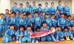 Children from Shiritsu Kahoku Kindergarten in Ishinomaki, Miyagi Prefecture, pose with a koinobori flag inscribed with inspirational messages from Washington State University students.